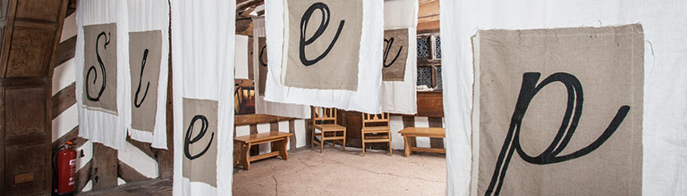 Sheets dividing a room with stitched letters spelling 'sleep' 